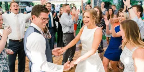 A bride and groom dancing at a wedding reception while surrounded by cheering guests.