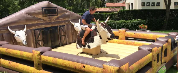 A person riding an inflatable mechanical bull attraction set up in a grassy outdoor area.