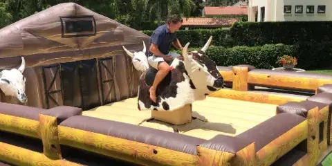 A person riding an inflatable mechanical bull attraction set up in a grassy outdoor area.