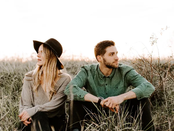 A professional photograph of a couple sitting in a field of tall grass during golden hour.