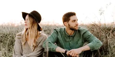 A professional photograph of a couple sitting in a field of tall grass during golden hour.