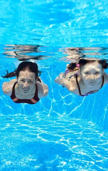 Two people swimming underwater in a bright blue pool.