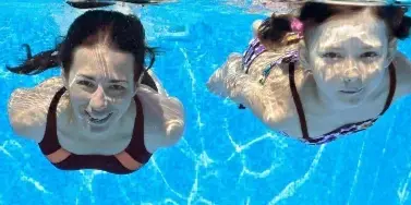 Two people swimming underwater in a bright blue pool.
