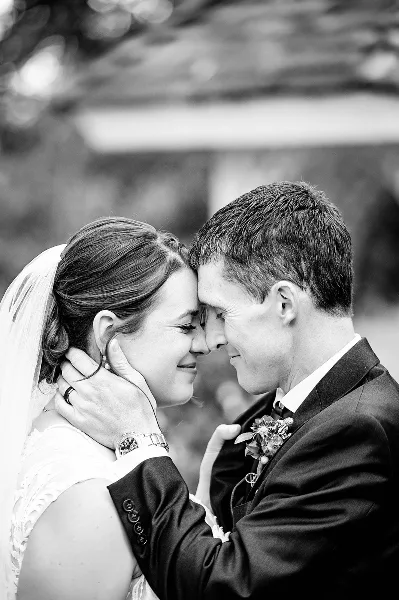 A black and white close-up portrait of a bride and groom touching foreheads and smiling at each other.