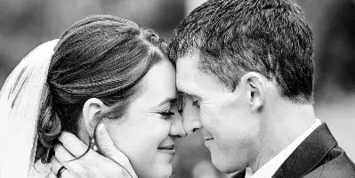 A black and white close-up portrait of a bride and groom touching foreheads and smiling at each other.