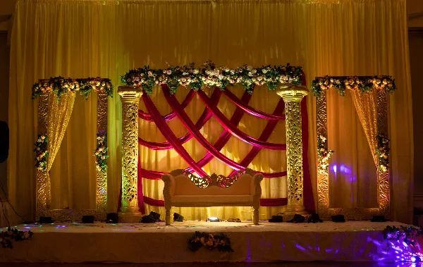 Decorated event stage with floral arch, gold pillars, and a white sofa