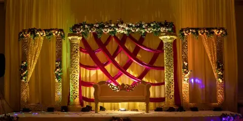Decorated event stage with floral arch, gold pillars, and a white sofa