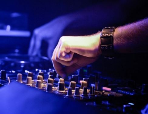 A close-up of a DJ's hands adjusting knobs on a mixing board under blue lighting.