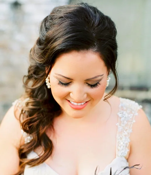 A bride with styled hair and professional makeup looking down while smiling.