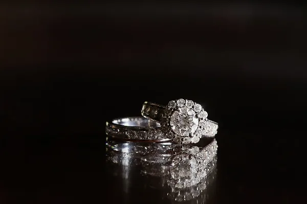 A professional photograph of a diamond engagement ring and a wedding band resting on a dark, reflective surface.