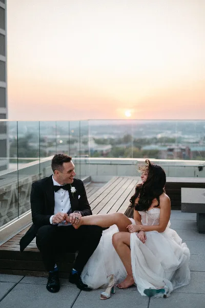 A bride and groom sitting on a rooftop terrace at sunset