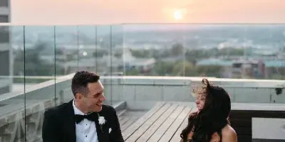 A bride and groom sitting on a rooftop terrace at sunset