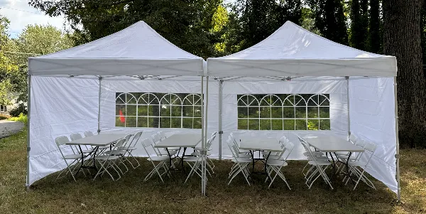 Two white canopy tents set up outdoors on a lawn, furnished with white folding tables and chairs.
