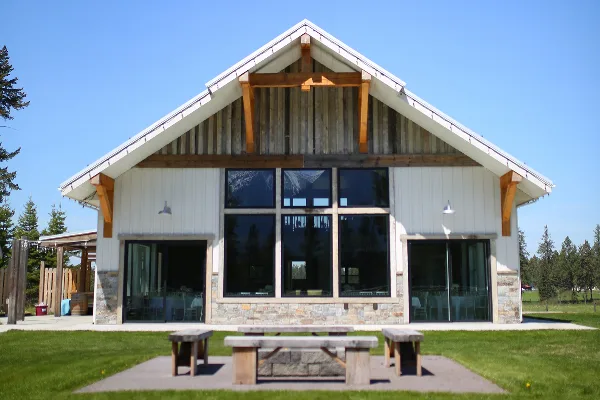 Exterior view of a modern wedding venue building with a steep gabled roof, exposed wooden beams, and large glass windows set against a blue sky.