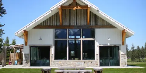 Exterior view of a modern wedding venue building with a steep gabled roof, exposed wooden beams, and large glass windows set against a blue sky.