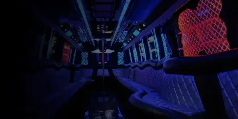 Interior view of a party bus featuring blue ambient lighting and white leather bench seating.