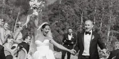 A black and white photograph of a bride and groom walking down the aisle at an outdoor mountain wedding ceremony.