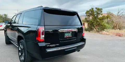 Rear view of a black GMC Yukon XL SUV with a custom '282RIDE' license plate, parked outdoors in a desert landscape.