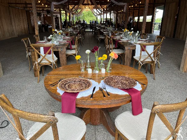 Interior of a wooden barn venue set up for a wedding reception with long tables, chairs, and floral centerpieces.