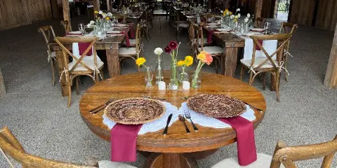 Interior of a wooden barn venue set up for a wedding reception with long tables, chairs, and floral centerpieces.