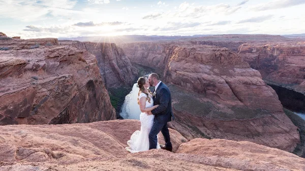 A bride and groom kissing on a rock ledge overlooking the Horseshoe Bend canyon.