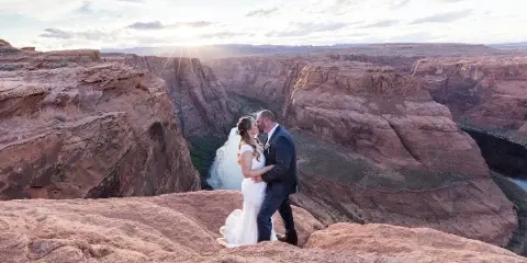 A bride and groom kissing on a rock ledge overlooking the Horseshoe Bend canyon.