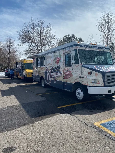 A white and blue mobile food truck branded with 'Capital City Wraps' parked in a lot.