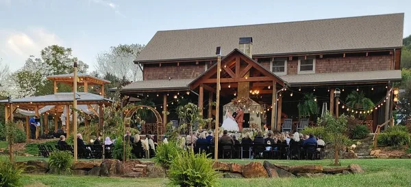 A wedding ceremony taking place on the covered porch of a large wooden venue building with guests seated in the foreground.