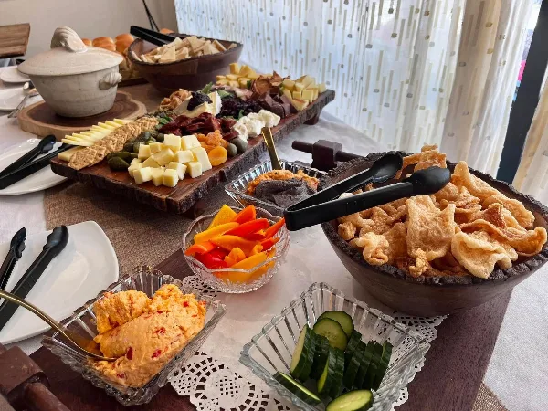 A catering table featuring a large charcuterie board, bowls of vegetable crudités, dips, and fried snacks set on a table with serving utensils.
