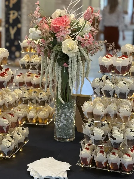 A tiered stand filled with assorted cupcakes and a floral centerpiece at a wedding event.