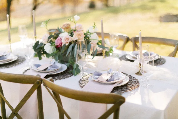 A professionally arranged outdoor wedding table featuring a floral centerpiece, white tablecloth, and elegant place settings.