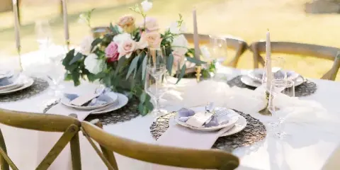 A professionally arranged outdoor wedding table featuring a floral centerpiece, white tablecloth, and elegant place settings.