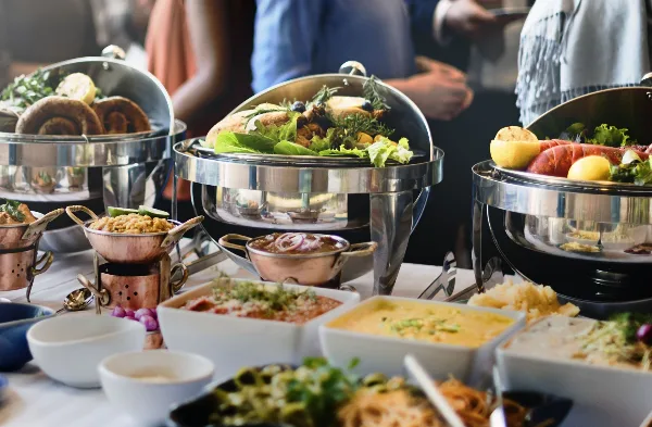 A catering table set with stainless steel chafing dishes, copper bowls, and various prepared food items including salads and breads.