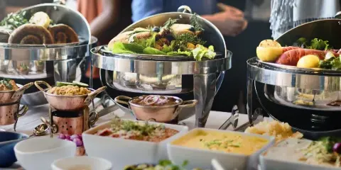 A catering table set with stainless steel chafing dishes, copper bowls, and various prepared food items including salads and breads.