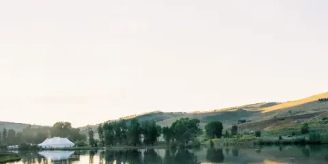 White event tent set up near a lake and rolling hills at an outdoor venue.