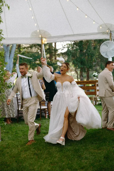 A bride and groom dancing joyfully at an outdoor wedding reception under a white tent.