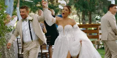 A bride and groom dancing joyfully at an outdoor wedding reception under a white tent.