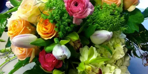 A lush floral arrangement containing peach roses, pink ranunculus, white tulips, green orchids, and white hydrangeas.