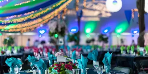 A decorated event table with teal napkins and glassware set up under a tent with string lights.