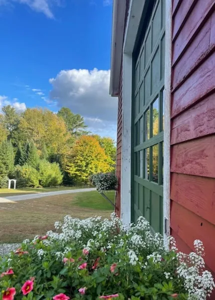 Exterior view of a red barn with green doors, surrounded by a lawn and autumn trees.