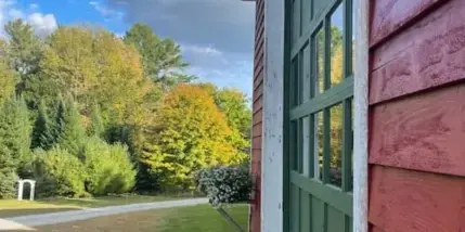 Exterior view of a red barn with green doors, surrounded by a lawn and autumn trees.