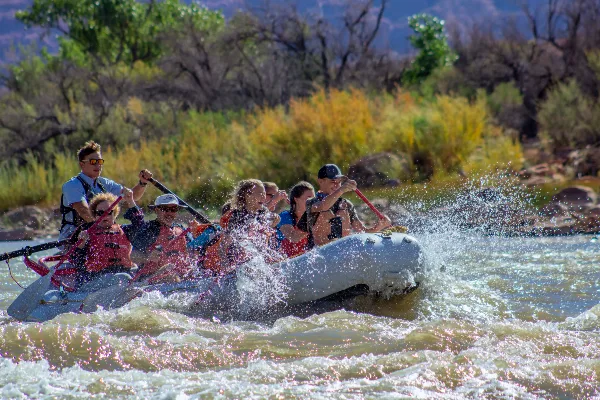A group of people in an inflatable raft paddling through whitewater rapids on a river.