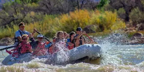 A group of people in an inflatable raft paddling through whitewater rapids on a river.