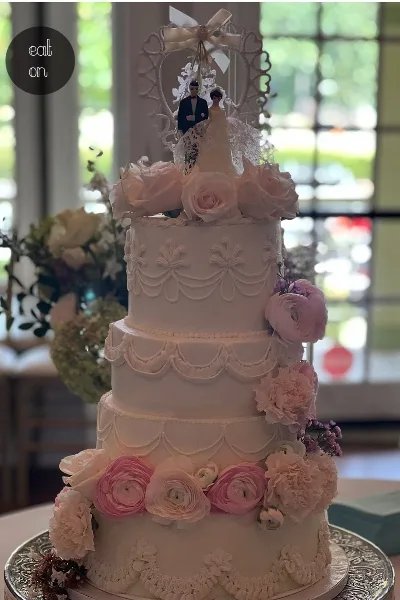 A three-tiered white wedding cake decorated with pink and white flowers and a bride and groom topper.