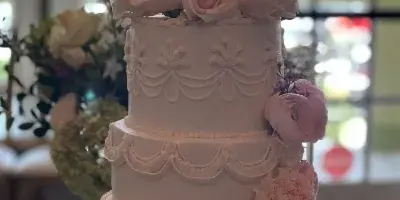 A three-tiered white wedding cake decorated with pink and white flowers and a bride and groom topper.