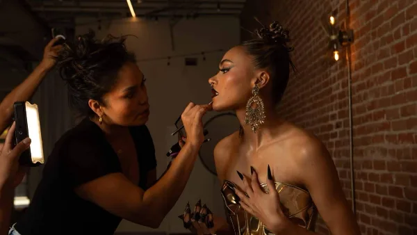 A makeup artist applying lipstick to a client in a studio setting.
