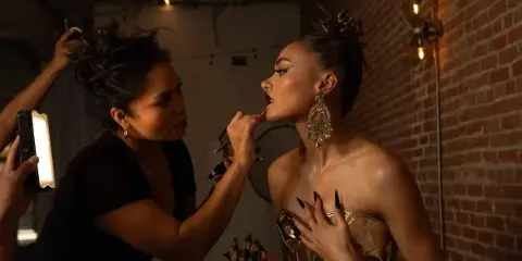 A makeup artist applying lipstick to a client in a studio setting.