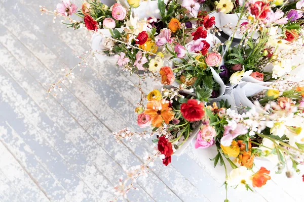 An assortment of colorful fresh flower bouquets wrapped in white paper, arranged on a light-colored wooden surface.
