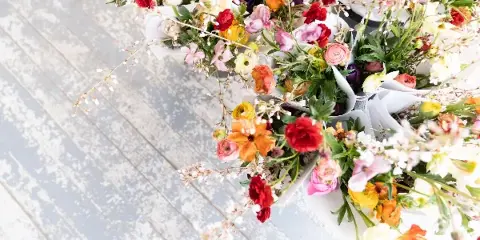 An assortment of colorful fresh flower bouquets wrapped in white paper, arranged on a light-colored wooden surface.