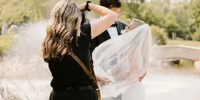 A photographer in black attire taking a picture of a bride and groom in a garden setting.